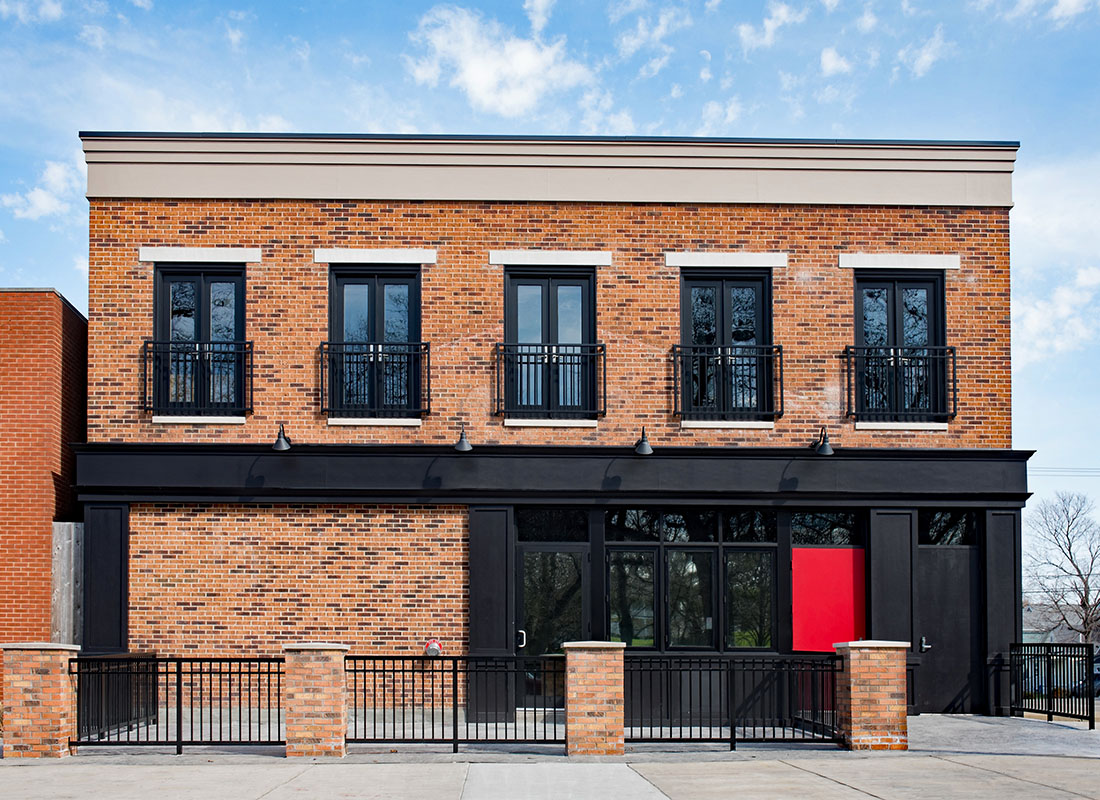 Business Insurance - Exterior View of a Red Brick Commercial Building on Main Street with Black and Red Accents on the Front Against a Cloudy Blue Sky
