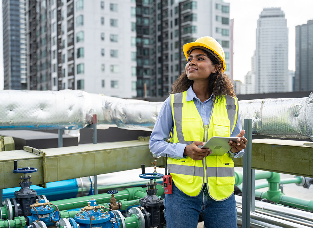 Insurance by Industry - Portrait of a Young Female HVAC Engineer Standing Next to Ducts and Cooling Equipment on the Roof of a Building in the City While Holding a Tablet