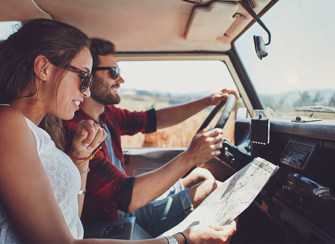 Personal Insurance - Closeup View of a Cheerful Young Couple Driving in a Jeep During a Road Trip While the Woman Looks at a Map